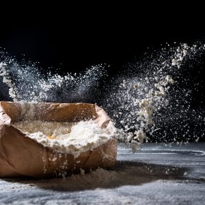 Bag with flour and egg flying in flour on black background. Flour splash. Cooking, baking concept