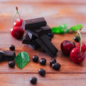 Dark chocolate in pieces isolated on wooden table with red cherries